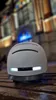 A smart helmet with LED lights sits on a wooden surface in front of a blurred building at night. Náhled obrázku produktu