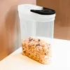 A clear plastic food storage container filled with granola sits on a white surface against a blurred background. Produktbild-Vorschau