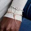 A close-up shot of a person's arm wearing two bracelets, one silver with charms and one rose gold with a pink stone. Anteprima dell’immagine prodotto