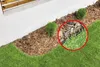 A garden bed with mulch and grass, bordered by a white wall. Produktbild-Vorschau