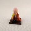 A small figurine of a meditating Buddha monk sits on a brown base. Produktbild-Vorschau