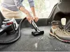 A person is vacuuming the trunk of a car with a Bosch handheld vacuum cleaner. A hiking boot is also visible in the trunk. Produktbild-Vorschau