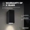 A black outdoor wall light mounted on a textured gray wall, with light illuminating downwards. Produktbild-Vorschau