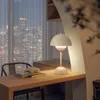 A desk with a lamp and books in front of a window with a city view at night. Produktbild-Vorschau