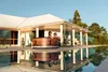 A couple relaxing in a wooden hot tub next to a swimming pool and a modern house. Náhled obrázku produktu