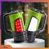Two green flashlights with black handles are displayed on a white pedestal against a blurred forest background. Podgląd zdjęcia produktu