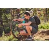 A man is kneeling next to a bicycle on a dirt trail, using a yellow tool on the rear wheel. Produktbild-Vorschau