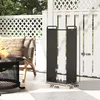A black metal firewood rack is shown on a patio next to a chair and a fire pit. Produktbild-Vorschau