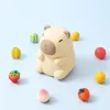 A cute, beige capybara-shaped night light sits in the center of a light blue background, surrounded by small, colorful fruit miniatures. Náhľad obrázku produktu