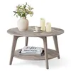 A round coffee table with a lower shelf, decorated with a vase of flowers, a teacup, and two candles on top, and books on the shelf. Produktbild-Vorschau