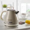 A cream-colored vintage electric kettle is displayed on a countertop, with cups of tea and tea bags in the background. Anteprima dell’immagine prodotto