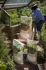 A woman is tending to a raised garden bed, with bags of soil and compost in the foreground. Produktbild-Vorschau