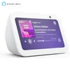 A white Amazon Echo Show 5 smart display is shown from a slightly elevated front-left angle, displaying music playback information on its screen. Produktbild-Vorschau