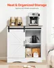 A white cabinet with a sliding barn door, displaying a coffee machine on top and various items inside, including coffee bags, a teapot, and mugs. Produktbild-Vorschau
