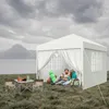 A couple relaxing inside a white gazebo next to a lake, with camping gear and a table with drinks. Voir les images du produit