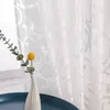 A close-up of a white sheer curtain with a damask pattern, next to a window with a small vase holding a single yellow flower. Produktbild-Vorschau