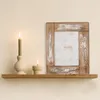 A wooden picture frame with a floral insert sits on a shelf next to two lit candles. Produktbild-Vorschau