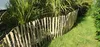A rustic wooden picket fence bordering a grassy lawn and lush green plants. Produktbild-Vorschau