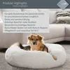A dog is lying in a round, fluffy white dog bed. The background shows a blurred living room setting with a sofa. Podgląd zdjęcia produktu