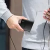 A person is putting a black power bank into the pocket of a gray hoodie. Produktbild-Vorschau