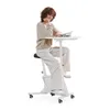 A woman is sitting on a stationary bike with a desk attached, reading a magazine. Podgląd zdjęcia produktu