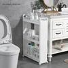 A narrow, three-tiered rolling storage shelf filled with various bathroom products is placed next to a toilet and a bathroom vanity. Produktbild-Vorschau