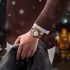 A man wearing a watch and sweater, holding a coat, with a blurred background of lights and a robot. Podgląd zdjęcia produktu