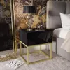 A bedroom scene featuring a black high-gloss nightstand with a gold metal frame, placed next to a bed. The background has a tropical flamingo-themed wallpaper and a large ornate mirror.