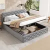A grey upholstered bed with its storage compartment open, revealing stored items. The bed is made of velvet fabric and has a diamond-stitched headboard. It is set in a room with light wooden flooring and a large window in the background. Náhľad obrázku produktu