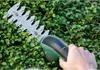 A hand holding a Bosch hedge trimmer cutting green bushes. Anteprima dell’immagine prodotto