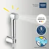 A chrome bidet spray is shown with water spraying from it, against a light gray background. Several marketing badges and text are present. Náhľad obrázku produktu