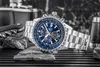 A watch is displayed on rocks with a flask and a corkscrew in the background. Produktbild-Vorschau