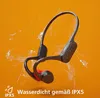 A pair of black and red bone conduction headphones are shown with water splashing around them against an orange background. Náhled obrázku produktu