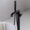 A black freestanding bathtub faucet with water running into a white bathtub. Náhled obrázku produktu