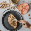 A slice of bread is being spread with pistachio cream, with pistachios, a jar of cream, and a flower in the background. Produktbild-Vorschau