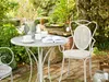 A white metal table and chair set on a patio with plants and a book on the table. Náhľad obrázku produktu