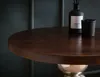 A close-up of a round wooden side table with a metallic base, featuring a diffuser and a candle on its surface. Voir les images du produit