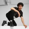 A young man is posing in a crouched position, wearing black Puma sneakers and a black and white t-shirt. Voir les images du produit