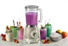 A vintage-style blender is shown in the center, surrounded by several colorful smoothies in glasses, a jar with a smoothie, and a bowl of crushed ice. Strawberries and apples are also visible. Produktbild-Vorschau