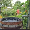 A rain barrel in a garden collecting water from a downspout. Produktbild-Vorschau