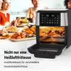 A family is enjoying a meal at a table, with an air fryer prominently displayed in the foreground, filled with food. Produktbild-Vorschau