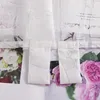 Close-up of white sheer curtains with a floral pattern and loops, layered over images of pink roses and white flowers. Produktbild-Vorschau