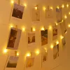 A string of fairy lights with photos clipped to them, decorating a wall. Produktbild-Vorschau