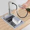 A person is using a pull-out faucet sprayer over a kitchen sink with dishes in a drying rack. Náhled obrázku produktu