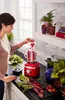 A woman is adding raspberries to a red blender in a kitchen. Produktbild-Vorschau