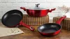 A set of red cookware, including two frying pans and a pot with a lid, is displayed on a wooden surface with a brick wall in the background. Náhled obrázku produktu