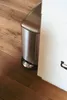 A stainless steel trash can is placed next to a white cabinet on a wooden floor. Produktbild-Vorschau