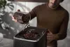 A man is pouring coffee beans into a coffee machine. Produktbild-Vorschau