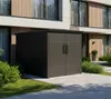 A dark gray metal shed with double doors is situated in front of a modern building, surrounded by green bushes and a paved walkway. Produktbild-Vorschau