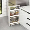 A white kitchen cart with four shelves filled with jars of food items is placed between a refrigerator and kitchen cabinets. Podgląd zdjęcia produktu
